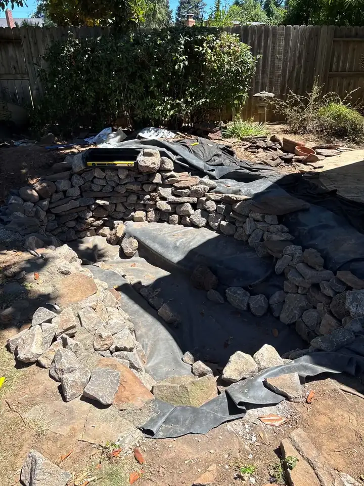 Backyard pond rebuild in progress with new liner and stacked stone waterfall wall